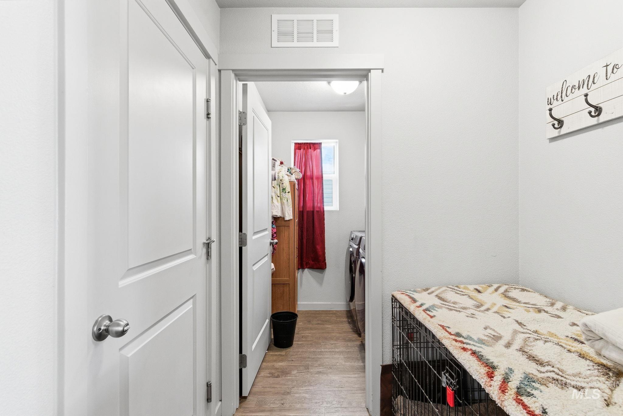 16887 Bethany Avenue Caldwell, ID 83607 - Photo 36 of 50 Interior hallway featuring white paneled doors, light grey wall paint, and wood-finish flooring extending into an adjacent room with a window
