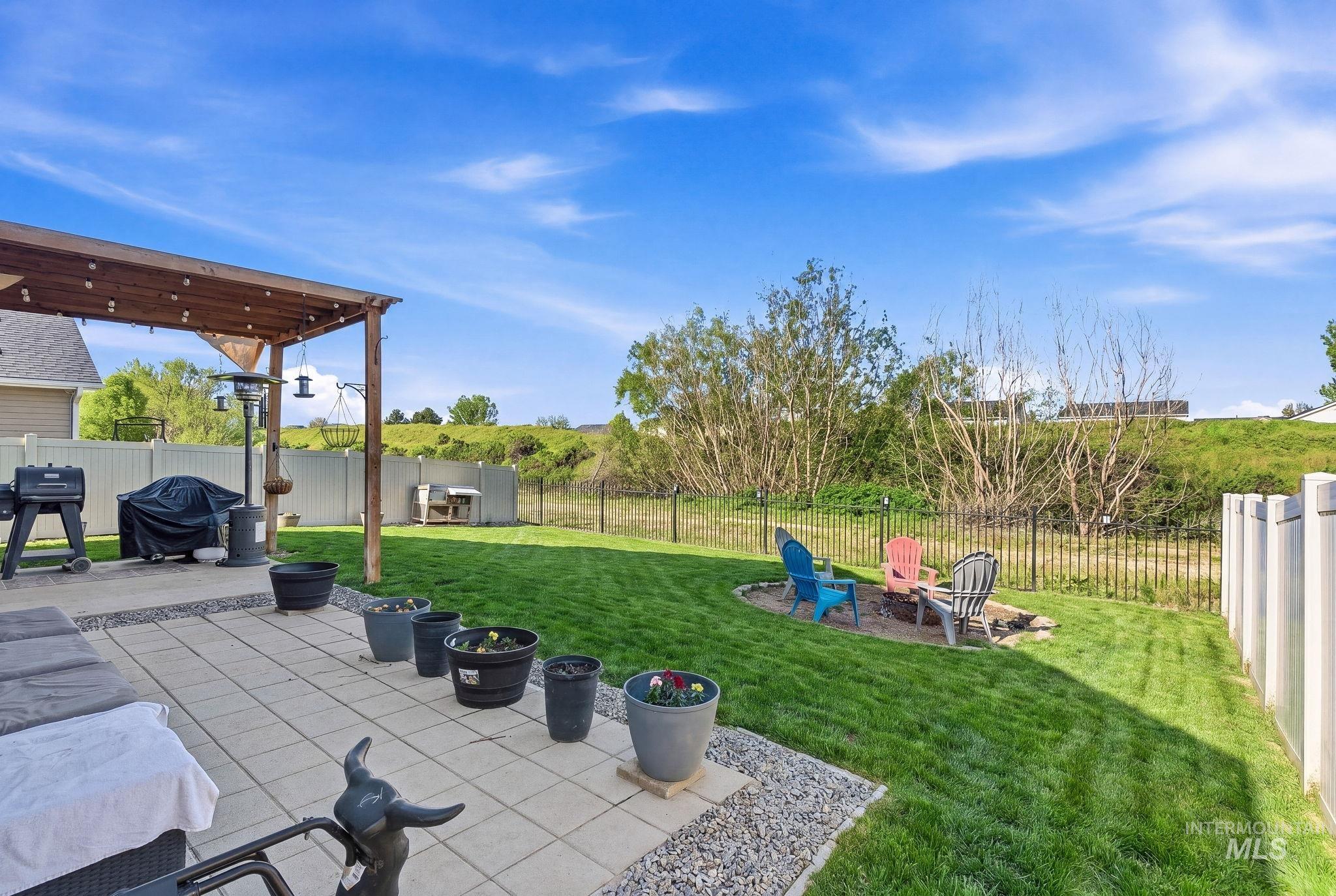 16887 Bethany Avenue Caldwell, ID 83607 - Photo 46 of 50 Expansive backyard featuring a paver patio with a wood pergola, green lawn, a fire pit area, and a combination of privacy and metal fencing