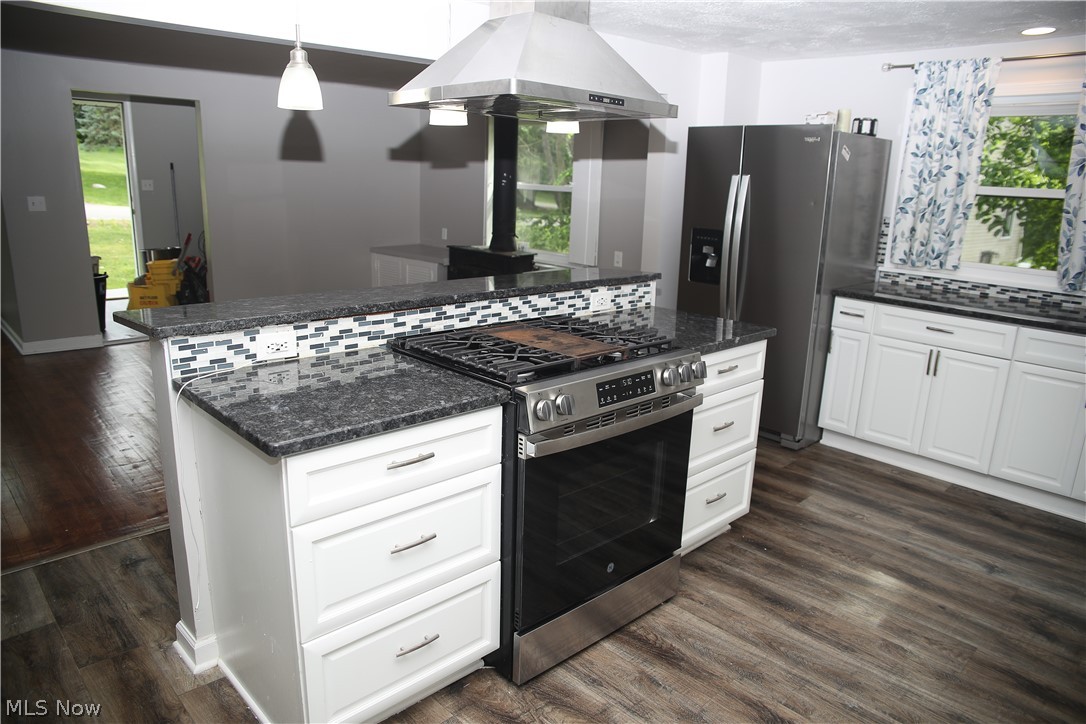 1087 Krumroy Road Akron, OH 44306 - Photo 14 of 23 Kitchen featuring an island with a built-in range, stainless steel appliances, granite countertops, a mosaic tile backsplash, and wood-finish flooring