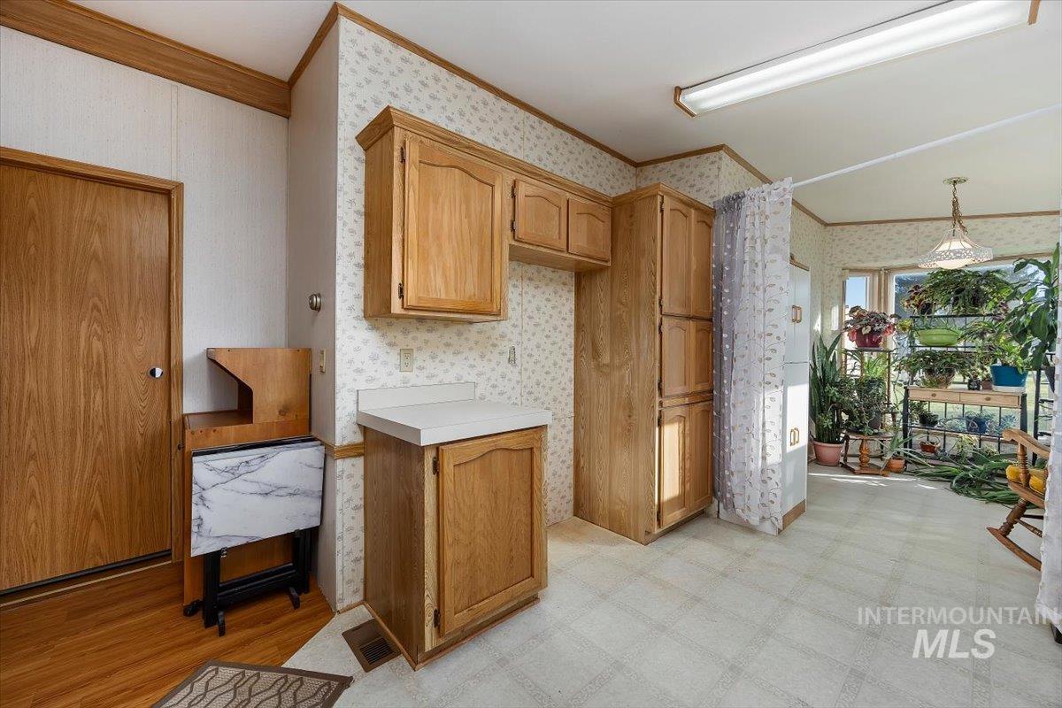 198 South Hills Road, Unit 142 Twin Falls, ID 83301 - Photo 13 of 27 Kitchen featuring light countertops, ornamental molding, light flooring, wallpapered walls, and brown cabinets
