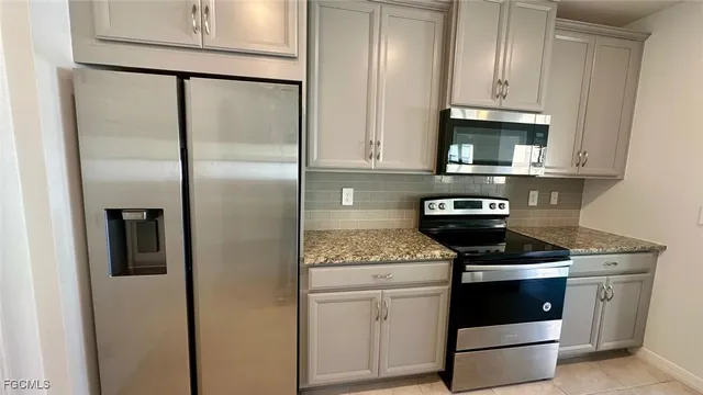 a kitchen with stainless steel appliances granite countertop a refrigerator a stove a sink and white cabinets