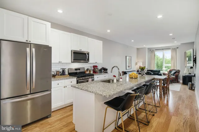 a kitchen with stainless steel appliances granite countertop a refrigerator a stove a sink a microwave a dining table and chairs with wooden floor