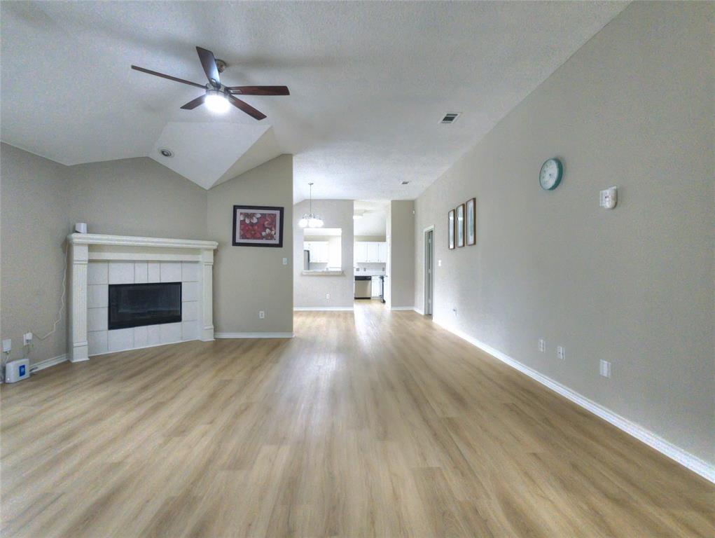 Spacious living area featuring wood-finish flooring, a white mantel fireplace with tile surround, and a ceiling fan