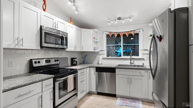 a kitchen with stainless steel appliances granite countertop white cabinets a sink a stove a refrigerator and a microwave