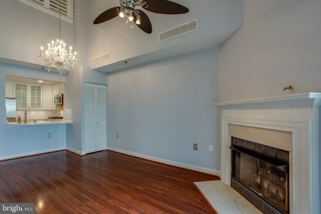 a view of an empty room with wooden floor and a kitchen