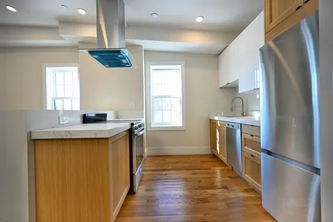 a kitchen with stainless steel appliances granite countertop a refrigerator a sink dishwasher a stove and a dining table with wooden floor