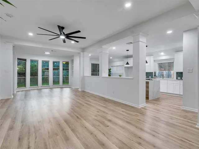 a view of an empty room with wooden floor and a kitchen