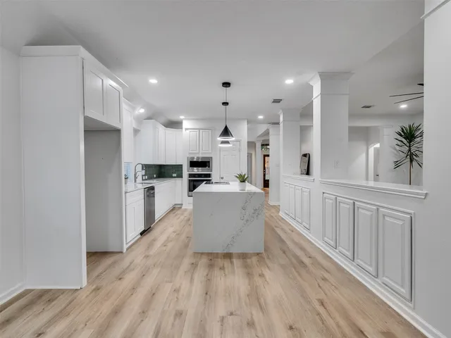 a large white kitchen with lots of counter space wooden floor and stainless steel appliances