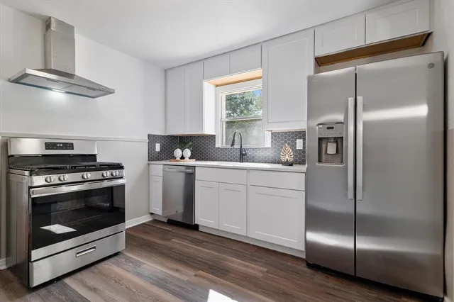 a kitchen with a refrigerator stainless steel appliances wooden floor and window