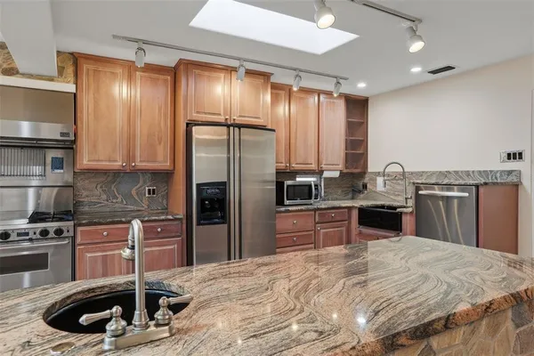 a kitchen with kitchen island granite countertop a sink stainless steel appliances and cabinets