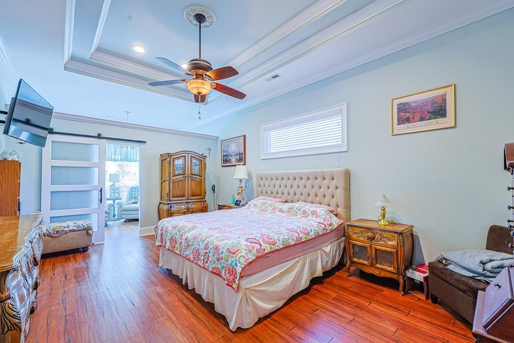 232 Waterfall Circle Little River, SC 29566 - Photo 12 of 40 Bedroom with a barn door, hardwood / wood-style flooring, ornamental molding, a ceiling fan, and a raised ceiling