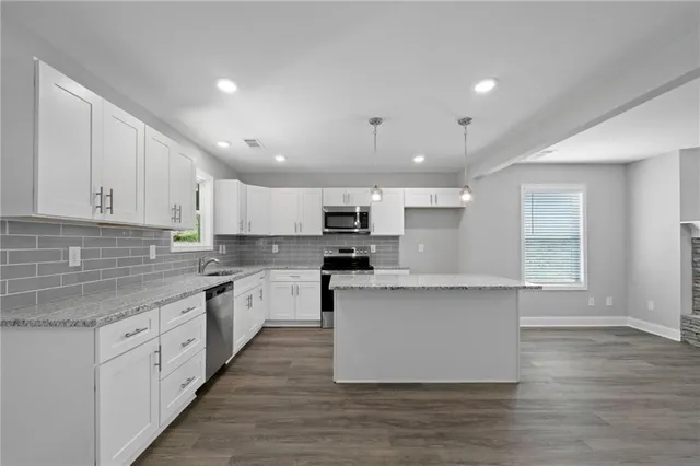 a large kitchen with stainless steel appliances granite countertop a stove top oven a sink and white cabinets