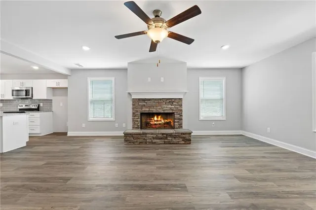 an empty room with wooden floor a ceiling fan a fireplace and windows
