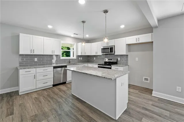 a kitchen with stainless steel appliances granite countertop a stove a sink dishwasher a refrigerator and white cabinets with wooden floor