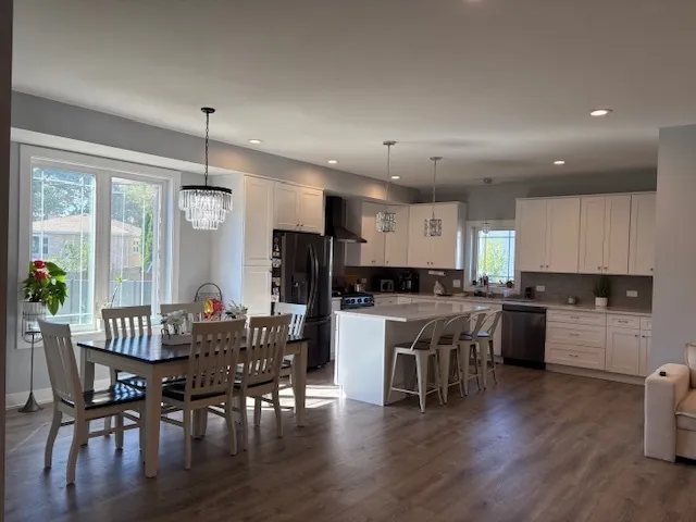 a kitchen with a dining table chairs wooden floor appliances and cabinets