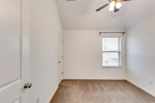 an empty room with chandelier fan and windows