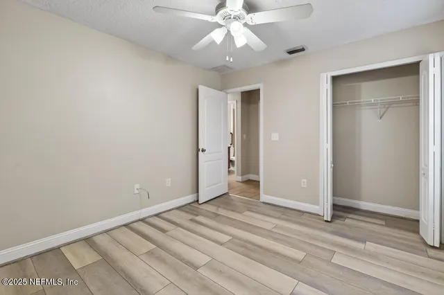 a view of an empty room with wooden floor and a ceiling fan