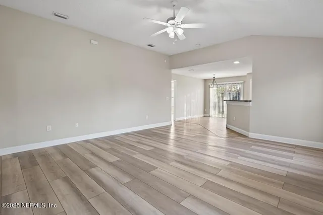an empty room with wooden floor and kitchen view