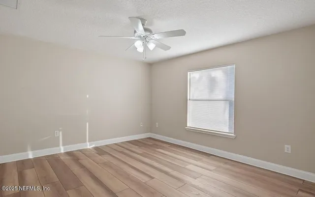 an empty room with wooden floor fan and windows