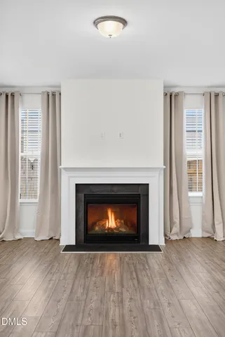 a view of an empty room with wooden floor fireplace and a window