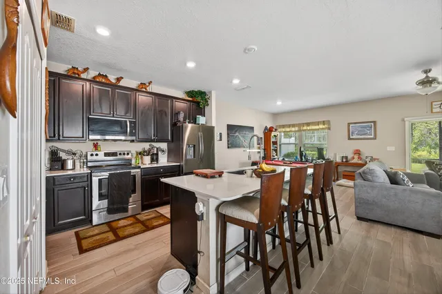 a kitchen with stainless steel appliances kitchen island granite countertop a refrigerator a stove a microwave oven a dining table and chairs with wooden floor