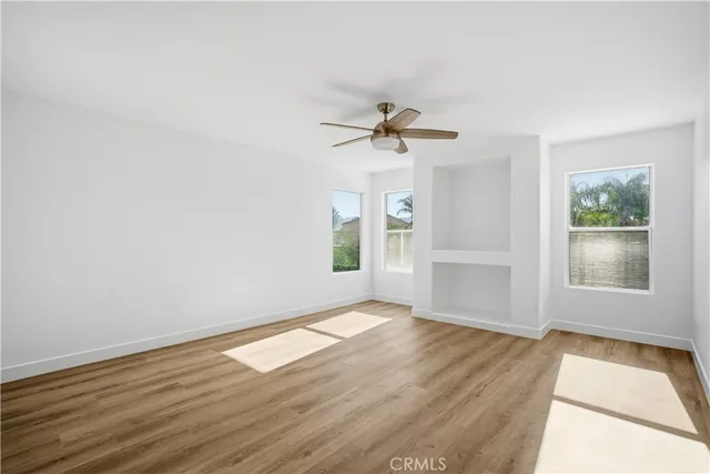 an empty room with wooden floor chandelier fan and windows