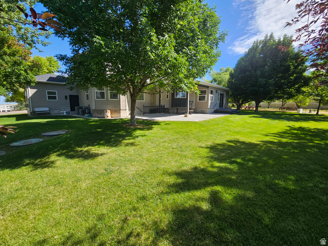 812 East Bates Cyn Road Tooele, UT 84074 - Photo 139 of 144 Expansive green lawn with mature shade trees, a concrete patio, and a light-colored stucco exterior