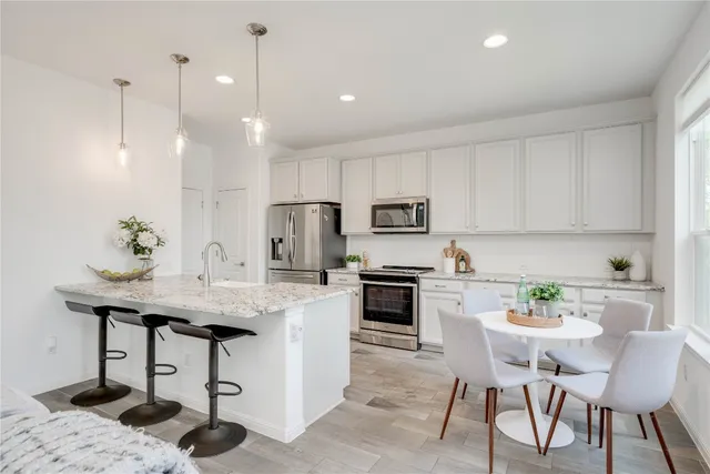 a kitchen with stainless steel appliances kitchen island granite countertop a table chairs stove and white cabinets