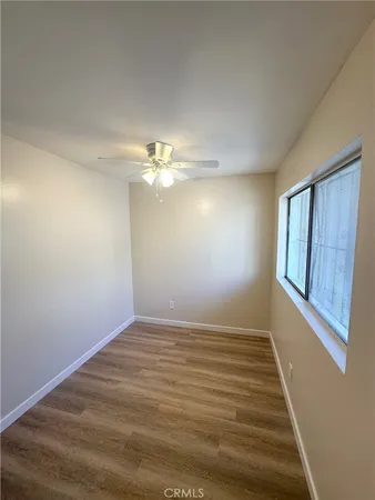 a view of an empty room with wooden floor and fan