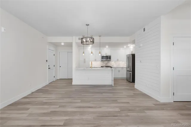 a kitchen with stainless steel appliances kitchen island granite countertop a refrigerator a sink dishwasher a stove and white cabinets with wooden floor
