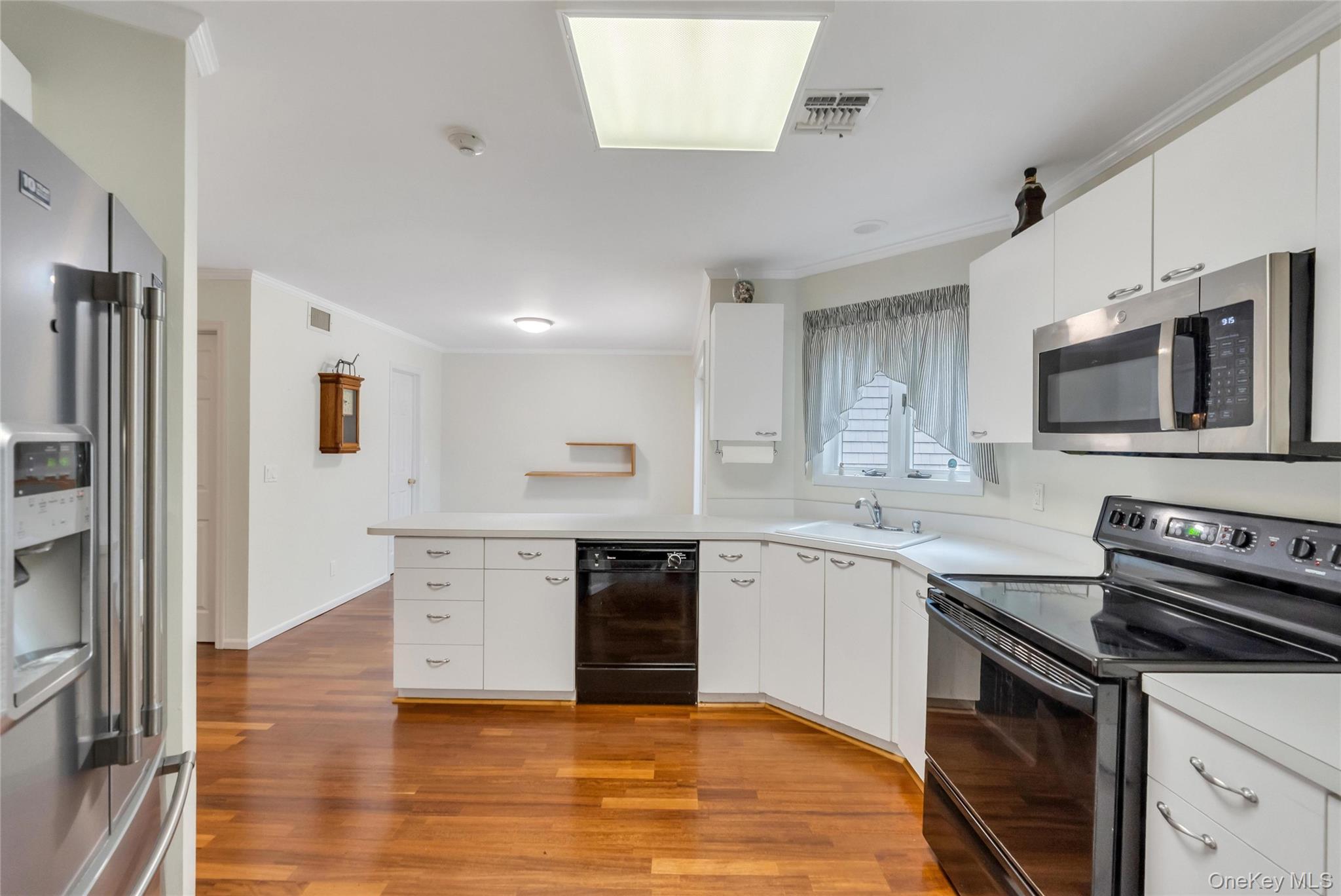 22 Kettle Hole Road Manorville, NY 11949 - Photo 11 of 39 Kitchen featuring wood-finish flooring, white cabinetry, and a suite of stainless steel and black appliances, including a built-in microwave, range, and refrigerator