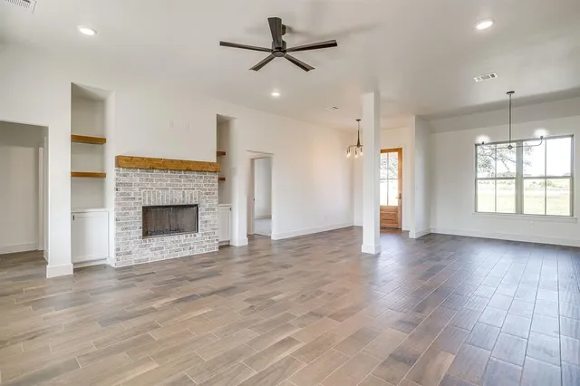 an empty room with wooden floor a ceiling fan a fireplace and windows