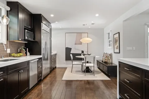 a kitchen with stainless steel appliances granite countertop a stove a sink dishwasher a refrigerator and a dining table with wooden floor