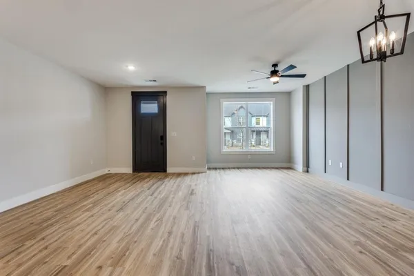 an empty room with wooden floor chandelier and windows
