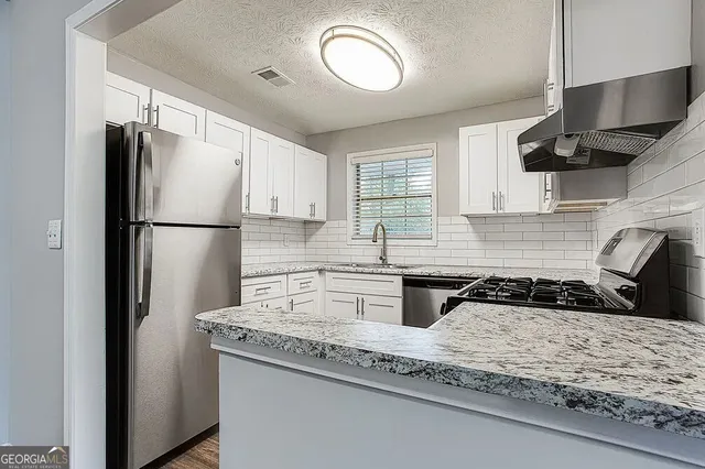 a kitchen with granite countertop stainless steel appliances a refrigerator a sink a stove and cabinets
