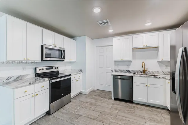 a kitchen with stainless steel appliances granite countertop a stove top oven a sink dishwasher a refrigerator and a oven with white cabinets