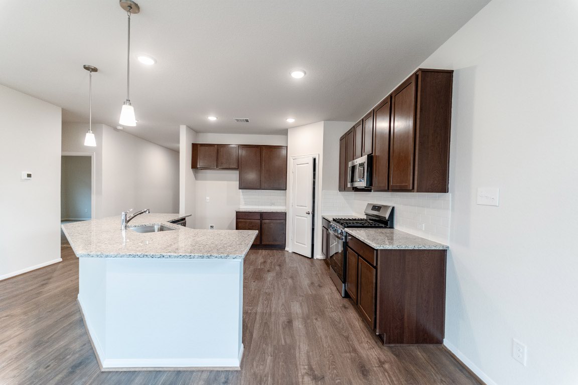 282 Denali Drive Kyle, TX 78640 - Photo 4 of 17 a large room with kitchen island a sink dishwasher a stove and a refrigerator with wooden floor