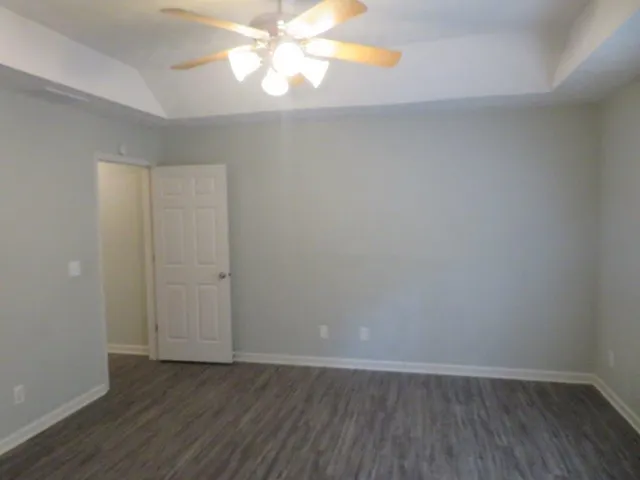 a view of an empty room with wooden floor and a chandelier fan