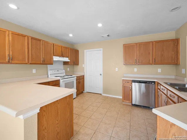 a kitchen with granite countertop a stove top oven a sink dishwasher and a refrigerator with wooden cabinets