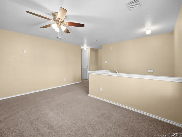 an empty room with a chandelier fan and kitchen view