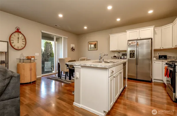 a kitchen with stainless steel appliances granite countertop a sink a stove a refrigerator and a dining table with wooden floor