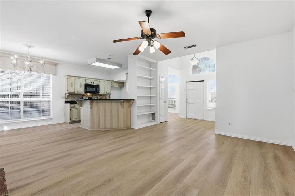 5023 Falcon Hollow Road McKinney, TX 75072 - Photo 9 of 25 Unfurnished living room featuring a chandelier, ceiling fan, light wood-style floors, and built in shelves
