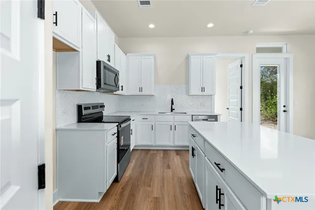 a kitchen with stainless steel appliances white cabinets a sink a stove a refrigerator and white cabinets