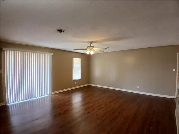 an empty room with wooden floor chandelier fan and windows