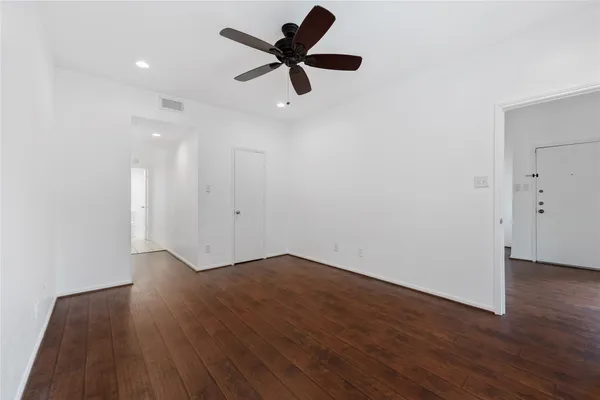 a view of an empty room with wooden floor and a ceiling fan