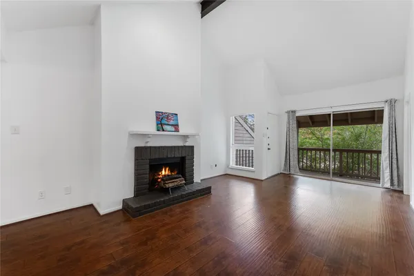 a view of an empty room with wooden floor fireplace and a window