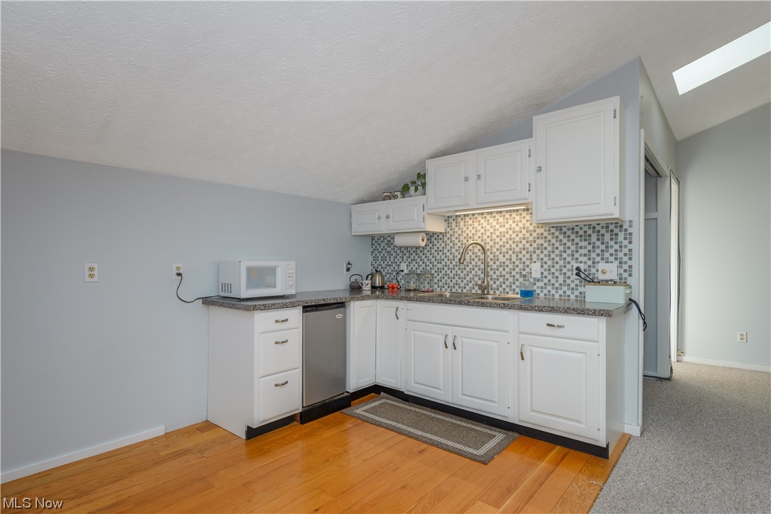 1049 North Medina Line Road Akron, OH 44333 - Photo 31 of 35 Kitchen featuring light carpet, tasteful backsplash, vaulted ceiling with skylight, and white cabinetry