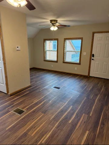 a view of an empty room with wooden floor and a window
