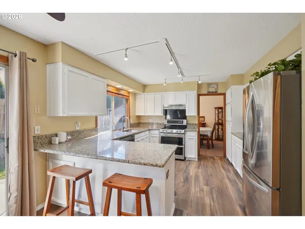 a kitchen with stainless steel appliances granite countertop a refrigerator a sink dishwasher a stove and white cabinets with wooden floor