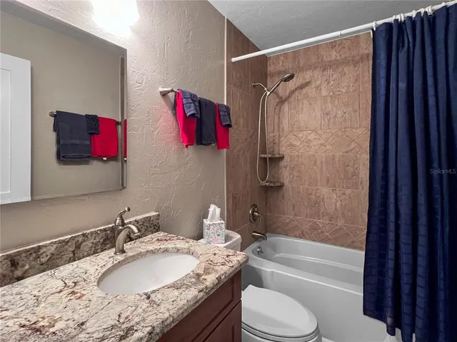 a bathroom with a granite countertop bathtub shower sink vanity mirror and toilet